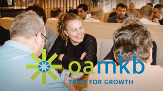 Groep mensen in gesprek tijdens een zakelijke bijeenkomst met oamkb logo en slogan ‘Tribe for Growth’ op de voorgrond